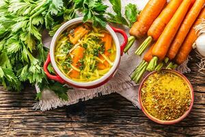 Chicken soup broth in a vintage bowl with homemade noodles carrot onion celery herbs garlic and fresh vegetables. photo