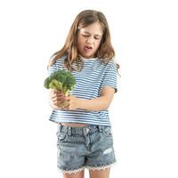 A little girl holds raw broccoli in her hand and looks at it with distaste. Isolated on white background photo
