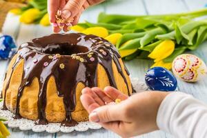 Delicious holiday slovak and czech cake babovka with chocolate glaze. Female hands decorating a cake .Easter decorations - spring tulips and eggs photo