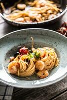 Pasta spaghetti on plate and pan with shrimp tomato sauce toatoes and herbs. Italian or mediterranean cuisine photo