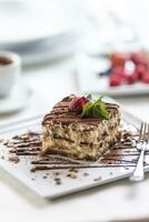 un cubo de Tiramisu postre servido en un de moda camino en un lámina, coronado con Fruta y menta foto