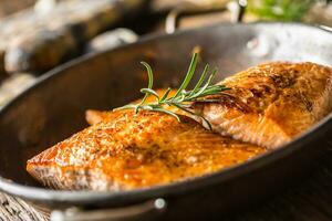 Salmon. Two juicy salmon steaks in roast pan with herb decoration on rustic oak table photo