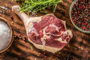 Top close-up view of a raw unskinned duck leg surrounded by pepper spice, rosemary herb and salt on a dark wooden background photo