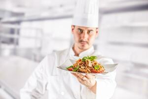 Chef in restaurant kitchen holding plate with italian meal spagh photo