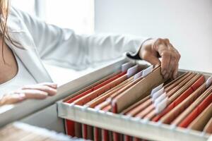 The clerk is leafing through stored folders, looking for a file or document. Concept of data storage, filing cabinet and business administration. photo