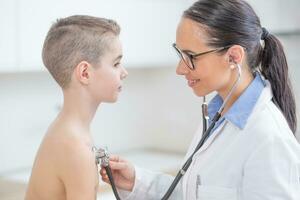 Young female doctor pediatrician examines boy patient with stethoscope photo