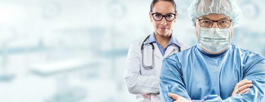 Male mid age surgeon in glasses wearing blue dress, protective face mask and hat, young female doctor in white dress with glasses and stethoscope standing with confidence in the back photo