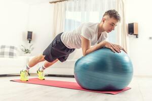 A young man exercises at home on a fitness ball photo