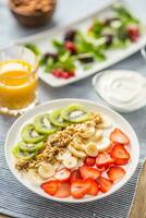 Healthy breakfast served with plate of yogurt muesli kiwi strawberries and banana photo