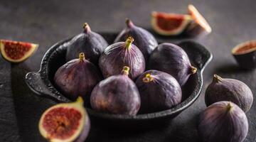 A few figs in a black bowl on an dark concrete table photo