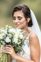 beautiful bride smells white wedding bouquet with eyes closed and a smile on her lips photo