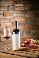 Cup and a bottle of red wine and raw beef steak on wooden table photo