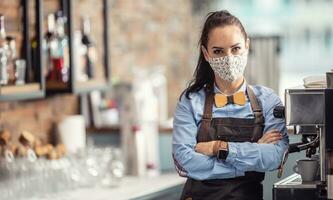 Female employee in a cafe stands unhappy with arms crossed wearing face mask photo