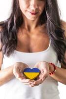 Brunette woman holding a Ukrainian heart carefully in her hands in fron of her chest. Representing love and emphaty to attacked people. Isolated background photo