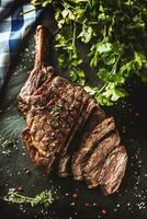 Freshly grilled tomahawk steak on slate plate with salt pepper rosemary and parsley herbs. Sliced pieces of juicy beef steak photo