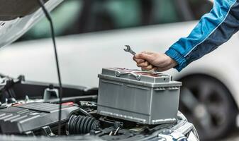 Mechanic holds key over car battery with engine trunk of the car open photo