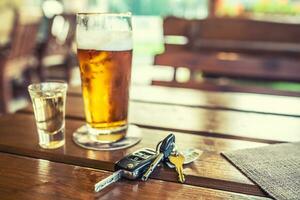 Car keys and glass of beer or distillate alcohol on table in pub or restaurant photo