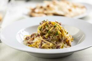 Spaghetti carbonara made with fried bacon cubes, yellow sauce from eggs and sprinkled with greens photo