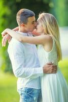 Young couple in love about to get a kiss, he holding her by the hips and she holding him around his arms. Dressed in white ona green nature background photo