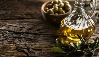 Glass bottle of olive oil and leaves with olives are designed on wooden table photo