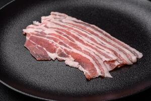 Fresh raw bacon cut into slices with salt, spices and herbs photo