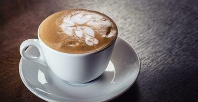 Cup of capuccino with rich decorative foam on top on a dark wooden table photo