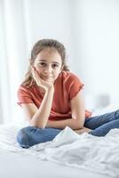 Young and confident pre-teen girl sits and leans on her hand looking into the camera photo