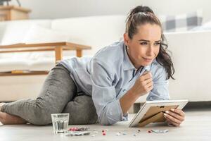 Young woman overdoses herself by pills on the living room floor holding a picture of someone whom she loved and lost photo