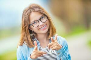 retrato de contento smilling Adolescente joven niña con lentes y hermosa sonrisa demostración con entusiasmo a usted foto