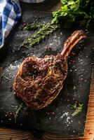 Freshly grilled tomahawk steak on slate plate with salt pepper rosemary and parsley herbs photo