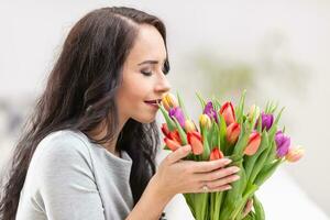 Dark haired woman smelling lovely aroma of fresh colorful tulips photo