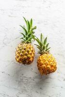 Two fresh whole pineapples with leaves on a marble surface photo