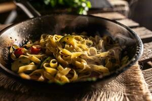 Vegetarian tagliatelle with zucchini and tomatoes served in sizzling hot pan photo