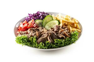 Isolated delicious Turkish veal kebab served on the white plate with fresh green letuce, juicy tomatoes, cabbage, cucumber and crispy and salty french fries photo