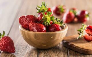 Juicy washed strawberries in wooden bowl on kitchen table photo