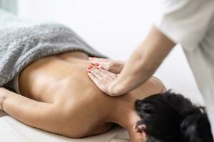 Woman masseur massages back of half-covered woman in the beautification studio photo