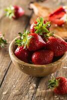 Juicy washed strawberries in wooden bowl on kitchen table photo