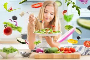 Young happy blonde girl eating healthy salad from arugula spinach tomatoes olives onion and olive oil. Healthy vegetable concept. photo