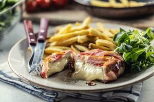 Cut melting cheese in a bacon wrap served on a plate with french fries and green salad photo