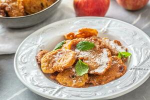 Finely fried apple pancakes sprinkled with vanilla sugar and cinnamon topped with mint leaves photo