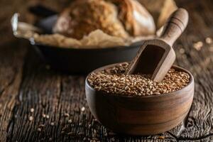 Wheat grains-the main ingredient of the bread filled in wooden bowl and wooden rustic scoop stitched deeply into. Bakend crusty bread in the backround photo