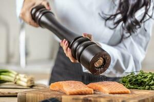 A salt grinder is used by a chef to season salmon in a restaurant kitchen photo