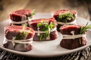 crudo carne de vaca filete cortes en un plato envuelto con instrumentos de cuerda y Fresco hierbas foto