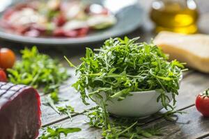 Fresh arugula salad in white dish on wooden table photo