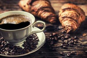 café. taza de café croissants y café frijoles. Clásico taza y antiguo roble mesa foto