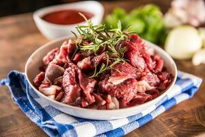Raw beef pieces with rosemary in bowl on butcher board photo