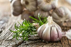 Garlic cloves and bulb with fresh rosemary on old wooden table photo