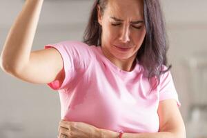 Woman can smell herself as she sweats with sweat patches in her armpits visible on a pink t-shirt photo