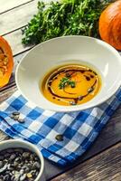 Pumpkin cream soup with seeds and parsley on kitchen table photo