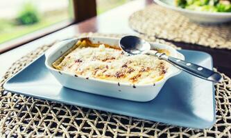 Portion of Lasagme bolognese in dish on table in restaurant photo